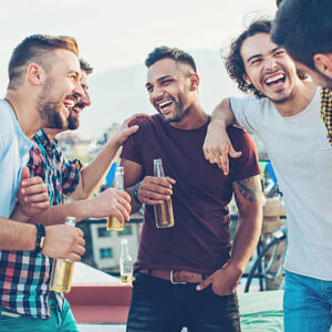 Multi-ethnic group of young men chatting and drinking beer on a rooftop party.